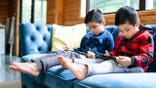 Two young boys sit on a couch using iPads.