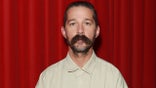 Shia LaBeouf poses in front of a red curtain
