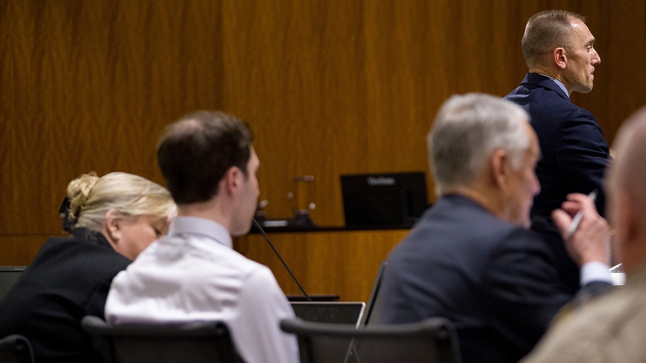 Ryan McBride standing and addressing a courtroom during a hearing.