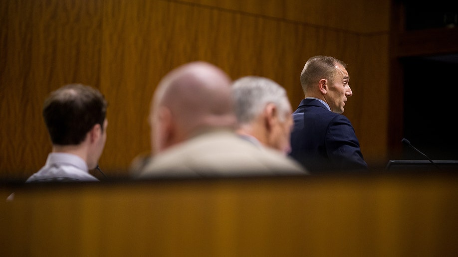 Ryan McBride standing and addressing a courtroom during a hearing.