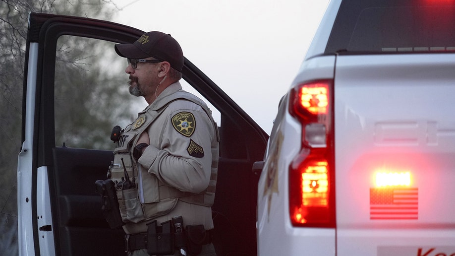 A member of the Pima County Sheriff's Department standing by a truck and looking towards Nancy Guthrie‘s house.