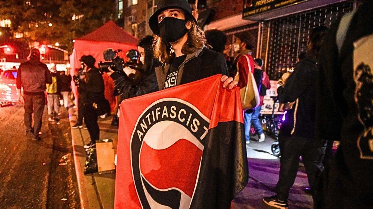Manifestantes mascarados seguram faixas da Antifa durante protestos noturnos em Nova York