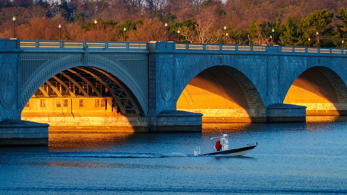 Sunrise illuminates the underside of the Arlington Memorial Bridge as a fishing boat cruises past on the Potomac River on March 23, 2025, in Washington, DC.