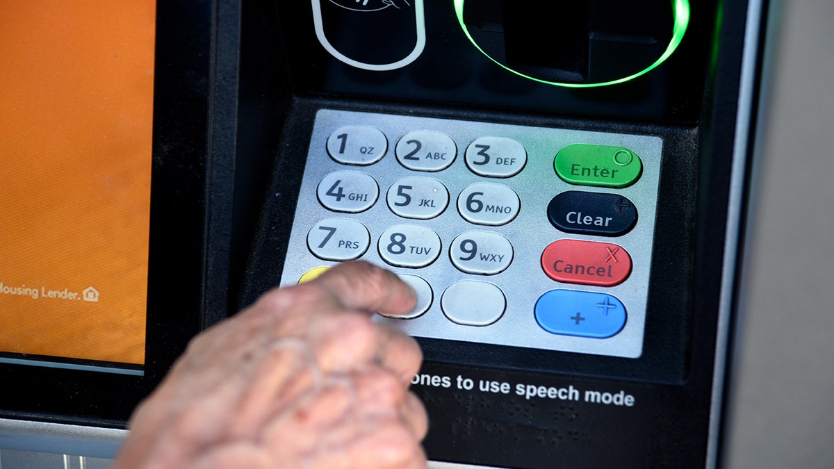 A person uses the pin pad on an ATM.