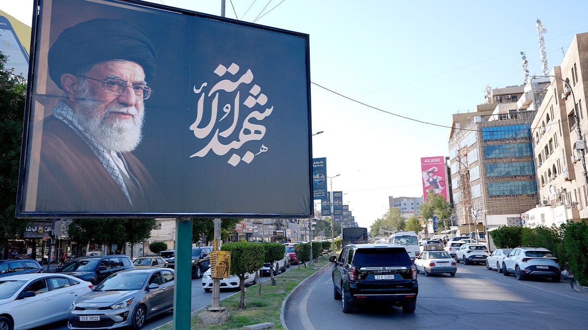 A large roadside billboard in Baghdad displays a portrait of Iran’s supreme leader above a city street.