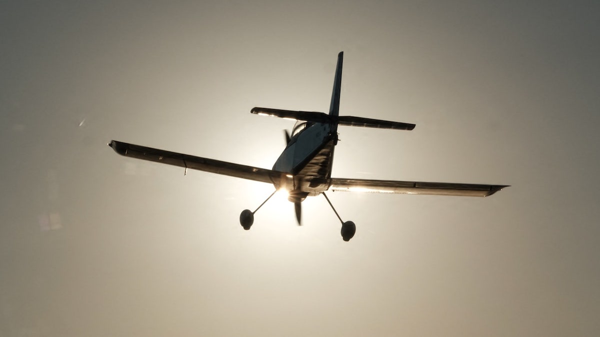a Beechcraft Bonanza plane flies against a sun drenched sky