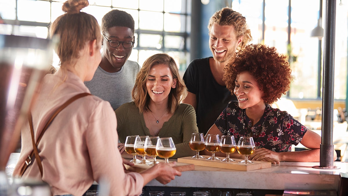 Waitress Serving Group Of Friends Beer Tasting In Bar