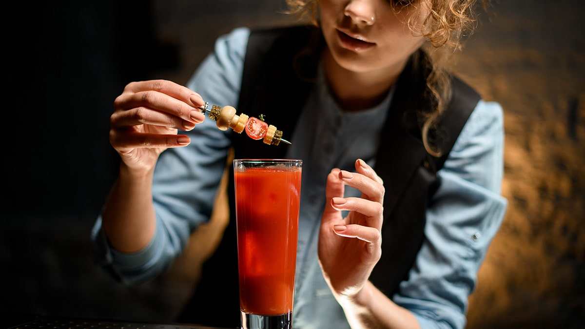 Il primo piano della barista decora con cura il bicchiere con il cocktail Bloody Mary con tartine e salsicce usando una pinzetta.