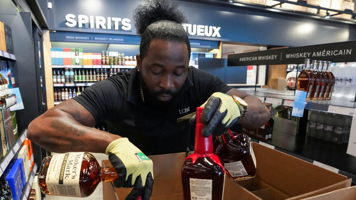 A shop worker in Canada removes U.S. alcohol from shelves in the wake of tariffs.