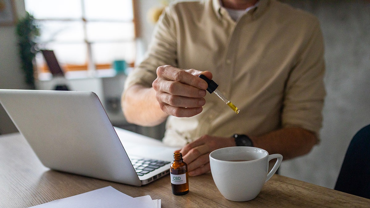 man drops cbd oil into a mug at his desk