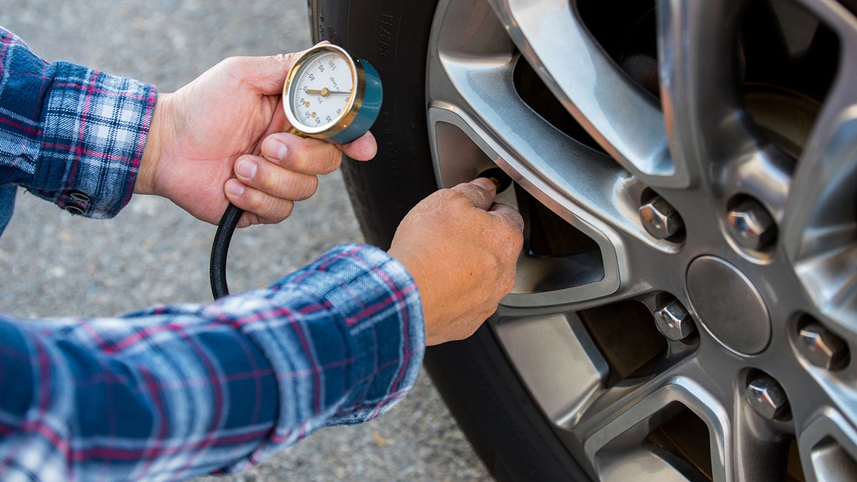 Close-up of man wearing plaid shirt checking tire pressure with guage.
