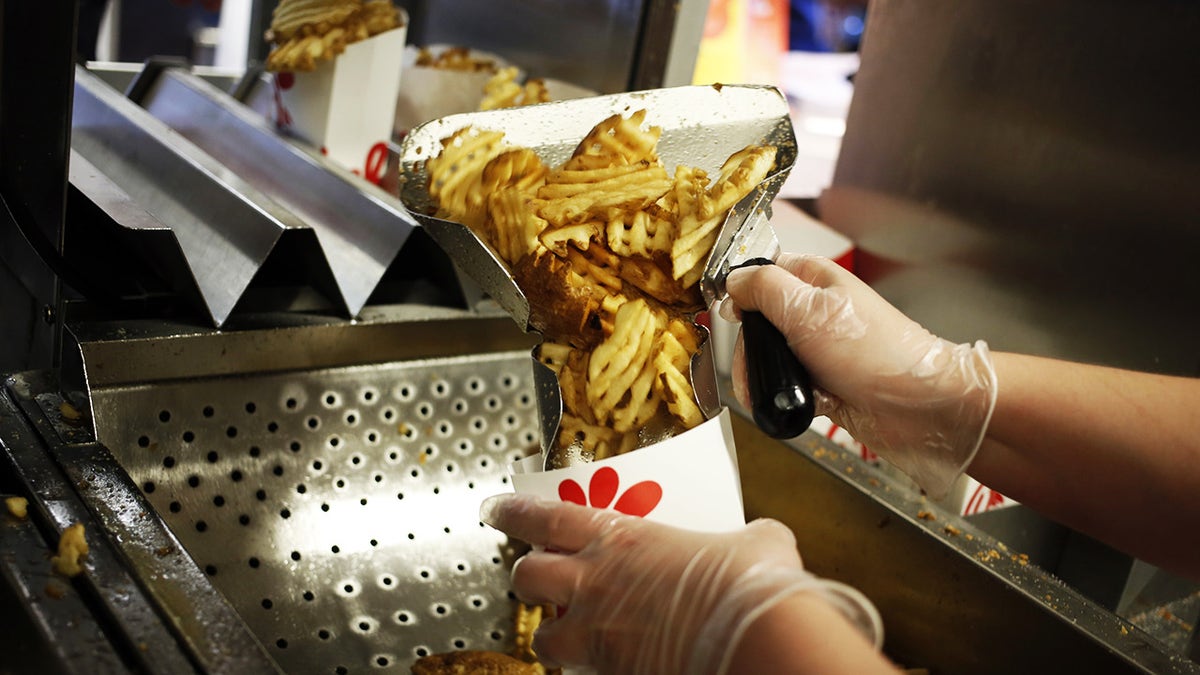 Chick-fil-A employee's gloves hands pouring waffle fries from fryer into serving cup.