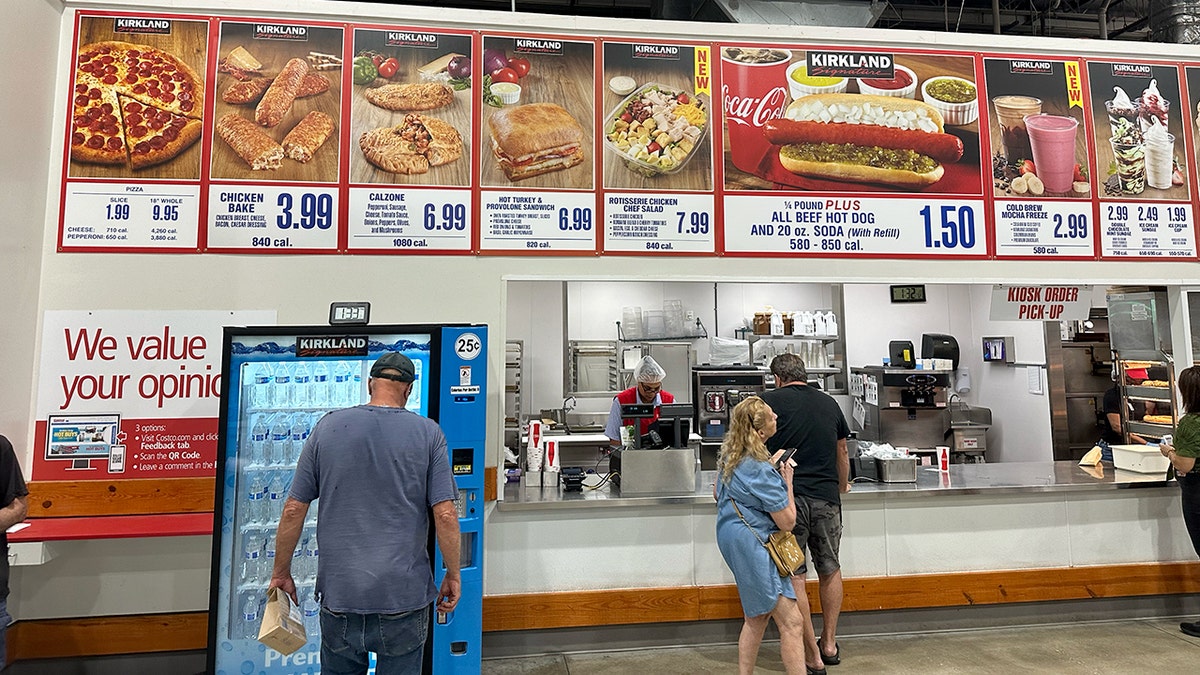 A customer looks at the Kirkland water bottles as other customers stand around the Costco food court.