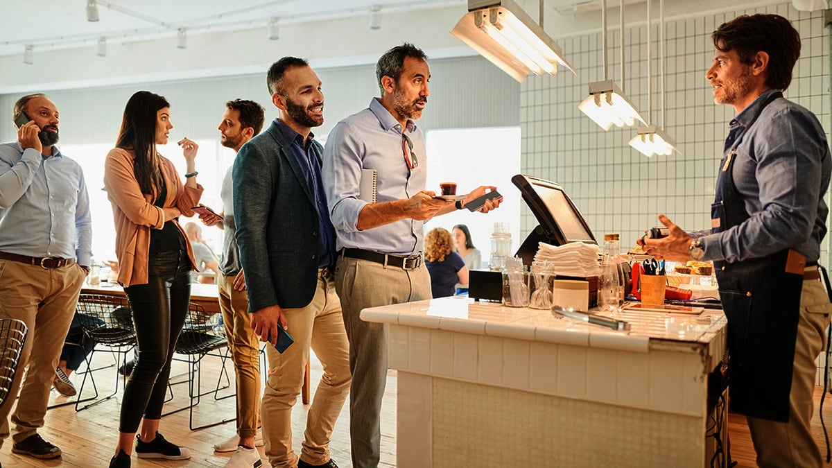 Line of people at cafe, including people on phones.