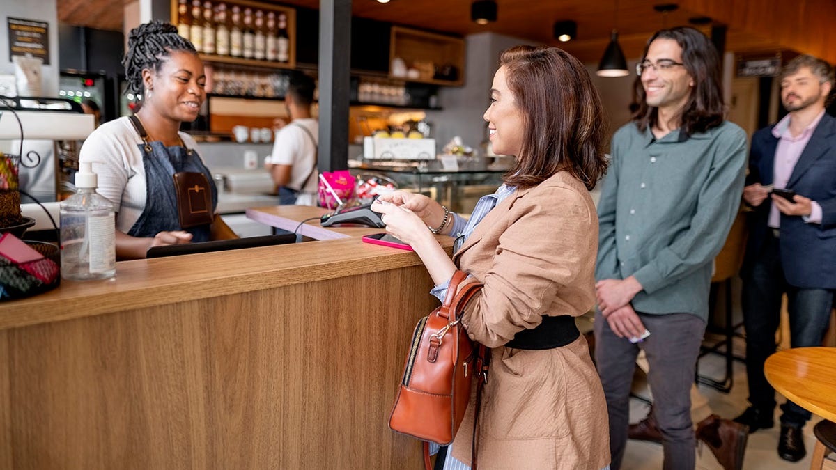.Businesswoman paying her bill at coffee shop checkout using credit card with people standing in queue behind her