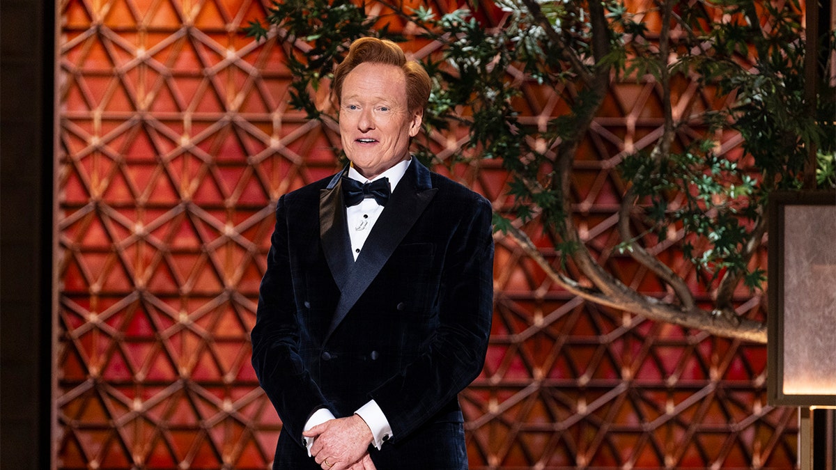 Conan O'Brien smiling and seated against a dark background