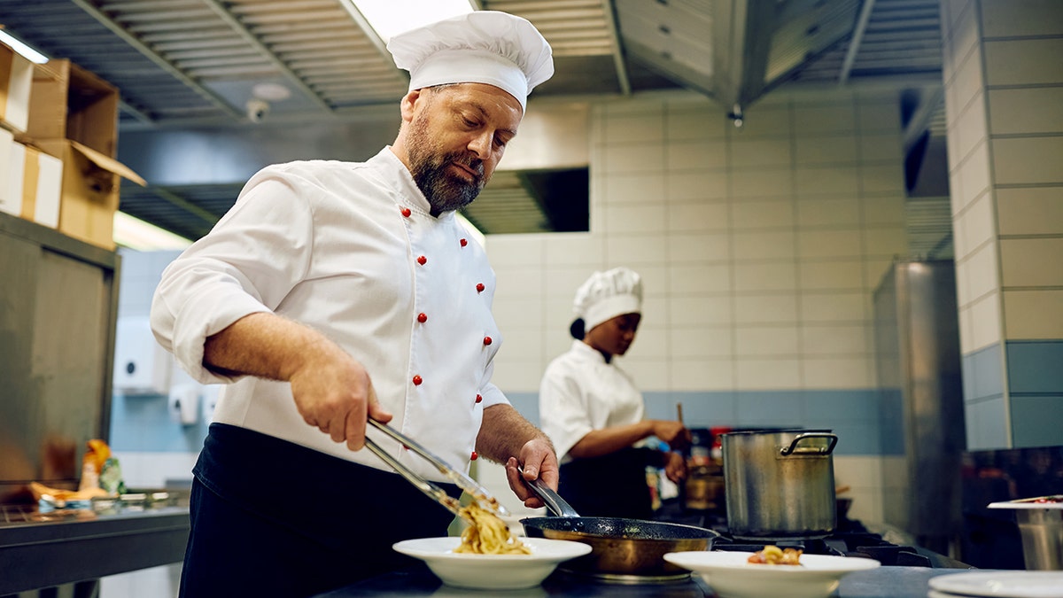 A male and female cook prepare dishes in a restaurant kitchen.