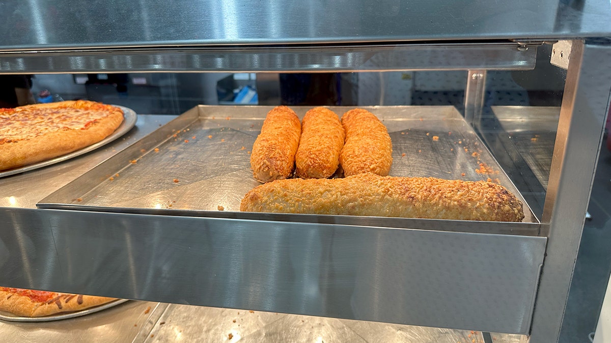 Four Costco Chicken Bakes are shown under the heating lights at the food court.