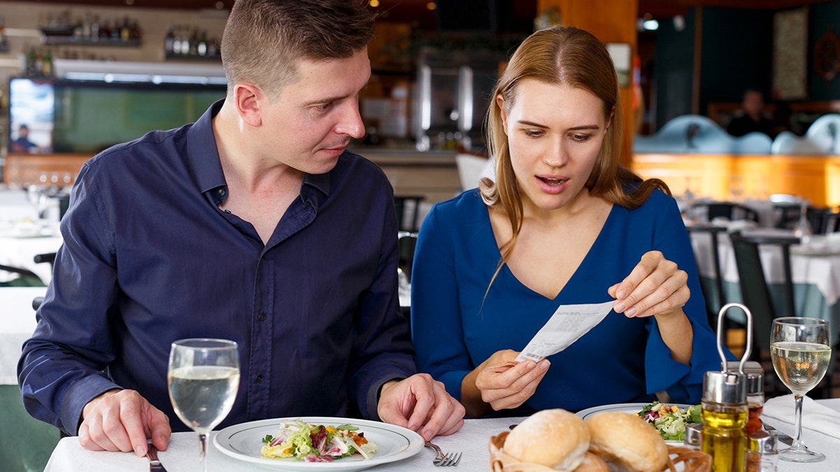 A man and a woman look at their check while seated at a restaurant table.