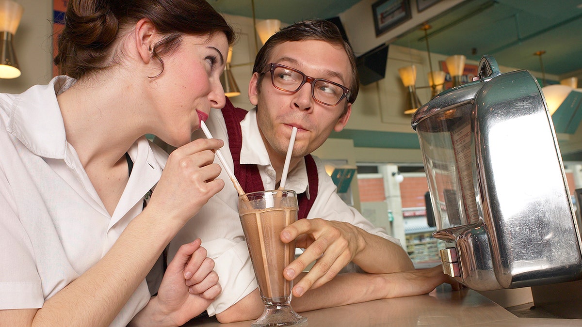 Retro couple sharing milkshake in diner.