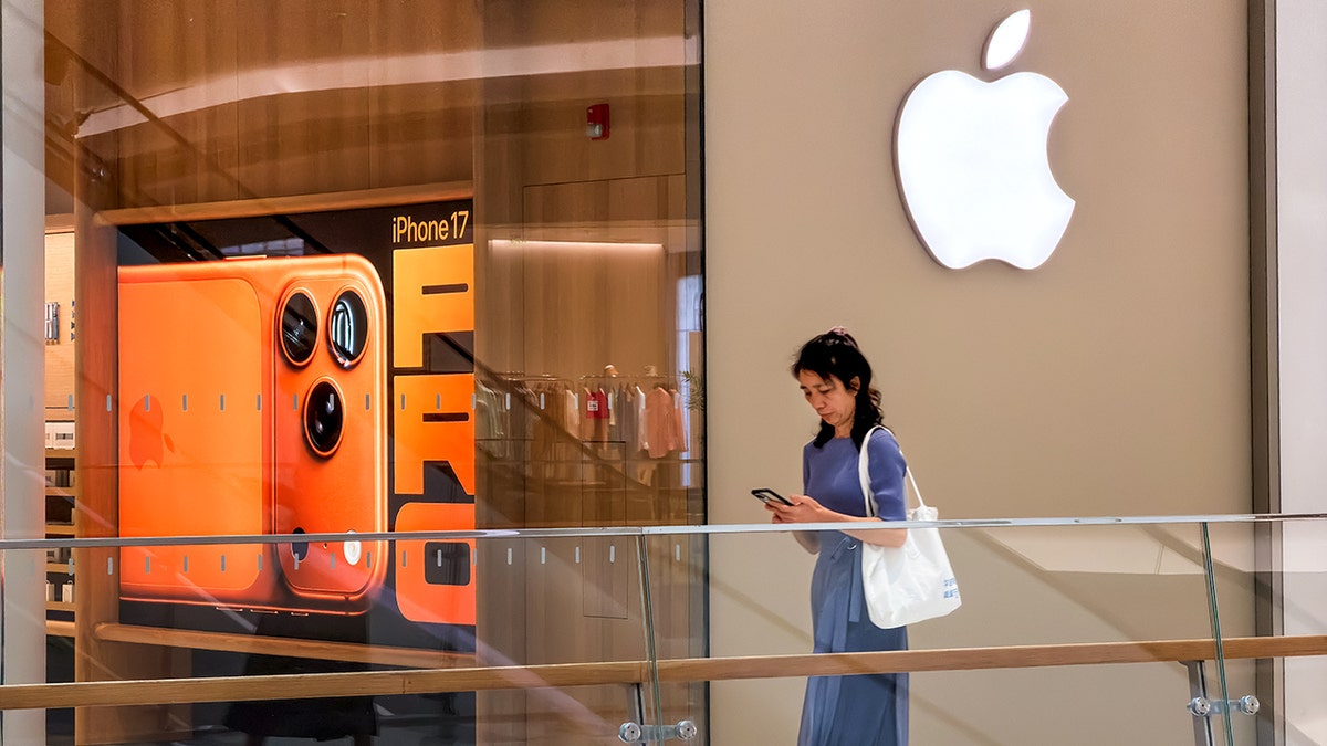 A woman walks past an Apple store, using her phone.