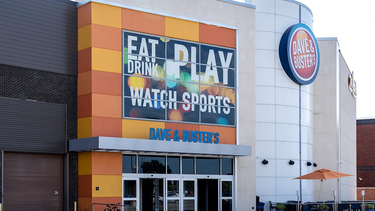 A large sign on the exterior of a Dave & Buster's restaurant says "Eat, Drink, Play, Watch Sports."