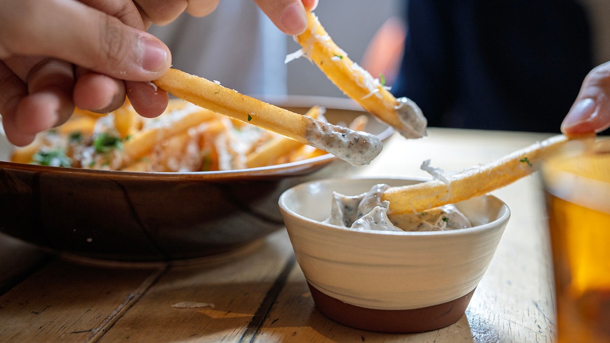 Friends dip truffle fries in creamy sauce.