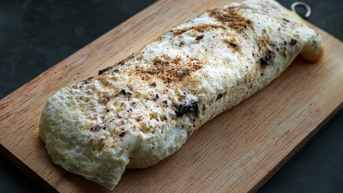 Egg white wrap stuffed with chicken breast and truffle sauce on wooden cutting board.