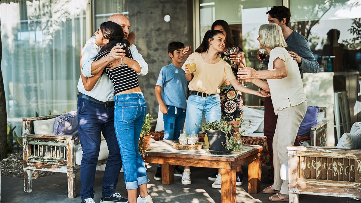 Grandfather embracing grandchild while having drink. Multi-generation family enjoying drinks at patio. They are celebrating during garden party.