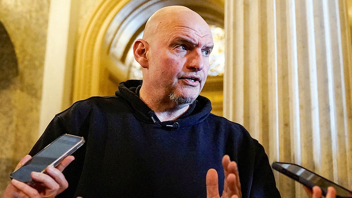 John Fetterman speaking into a group of cell phones held by media members.
