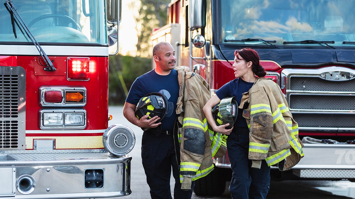 male and female firefighters talk while holding their gear