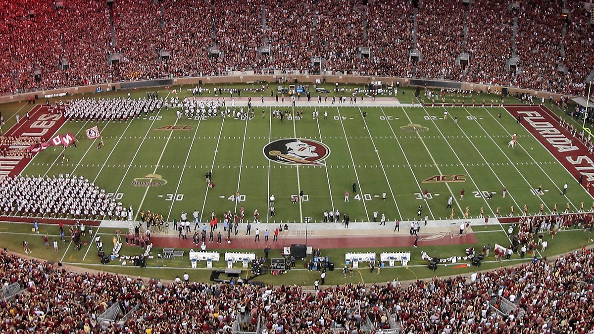 Jogadores de futebol americano do Florida State Seminoles correndo para o campo com fogos de artifício no alto