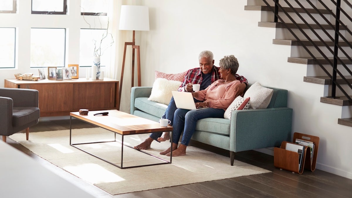 Senior Couple Sitting On Sofa At Home Using Laptop To Shop Online