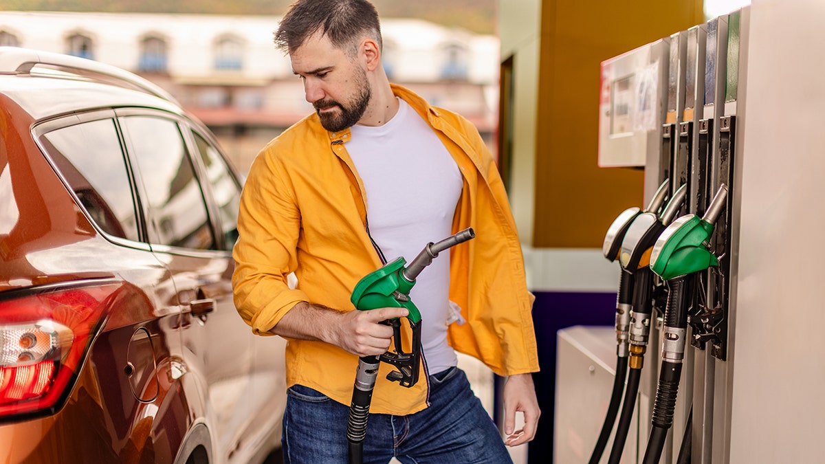 A man in a bright shirt refueling his brown car at a gas station during the day