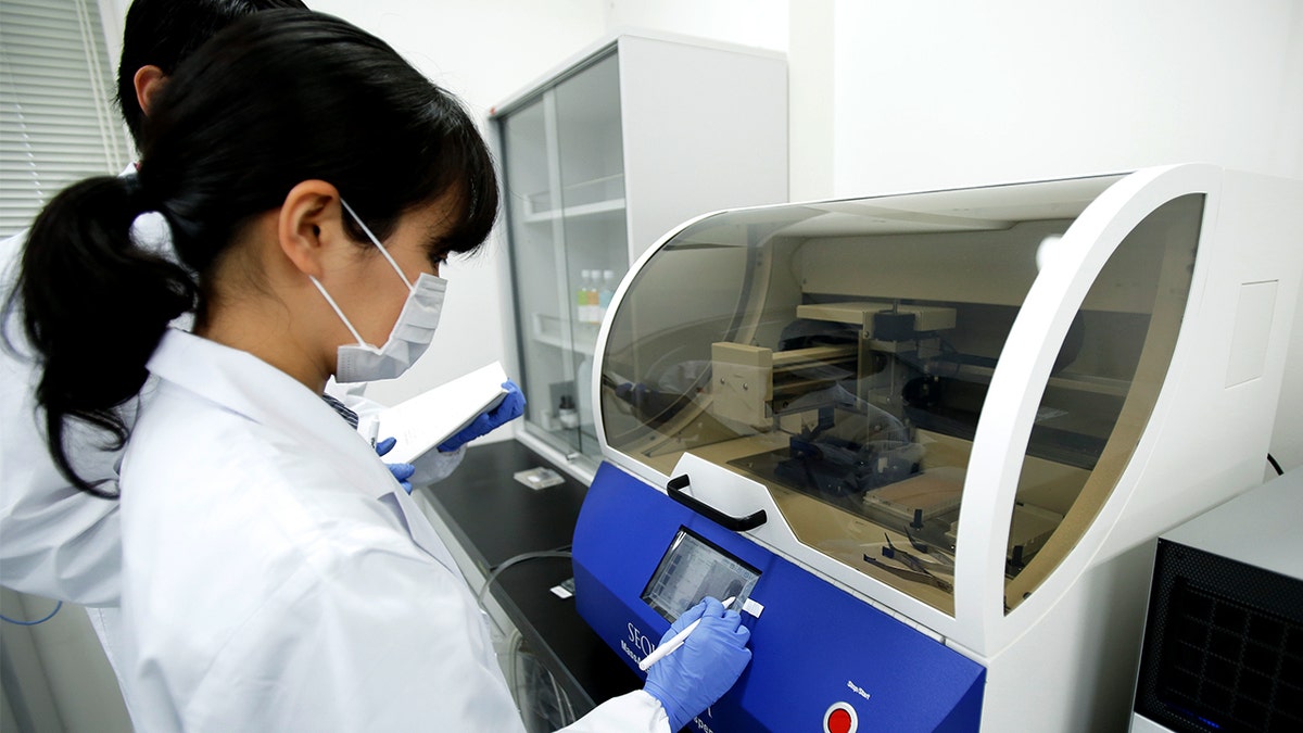 Uma mulher com um jaleco branco ajusta as configurações de um dispositivo em um laboratório.