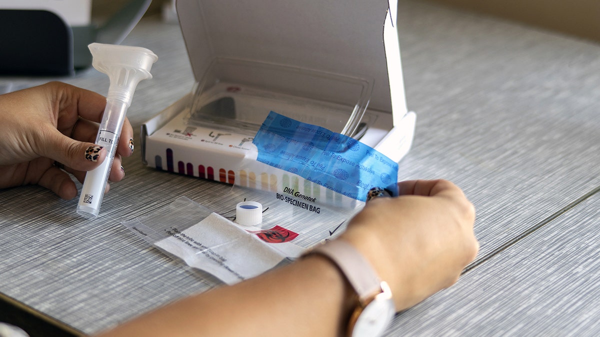 A person holds items from a DNA testing kit.