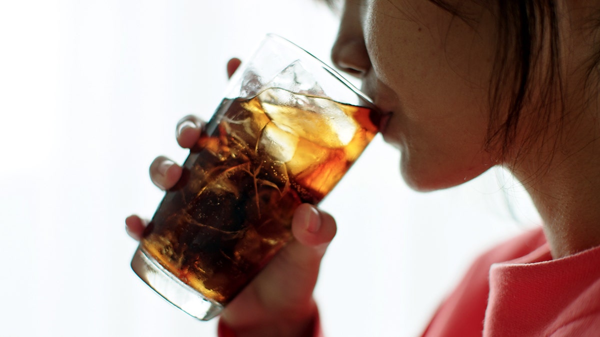 Teenage girl drinking cola from a glass with ice.