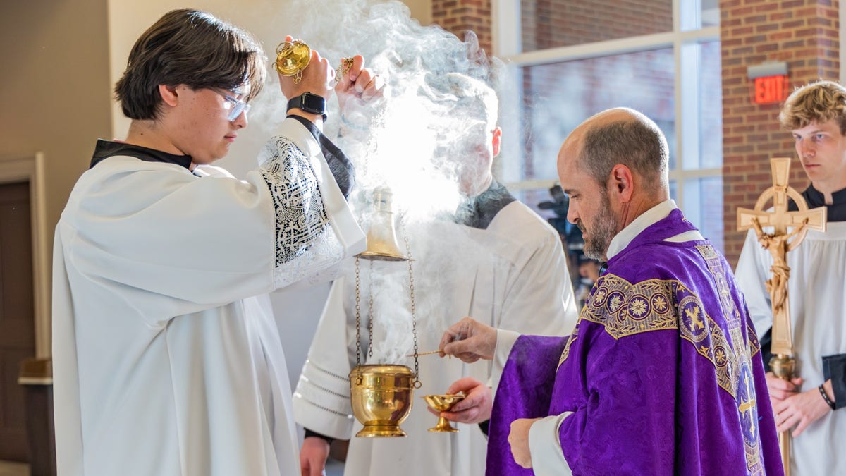 Priest and alter server at Catholic mass light incense