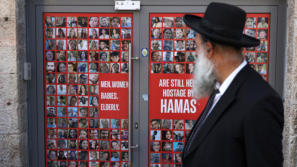 Um refém israelense passa por uma faixa com retratos de israelenses.