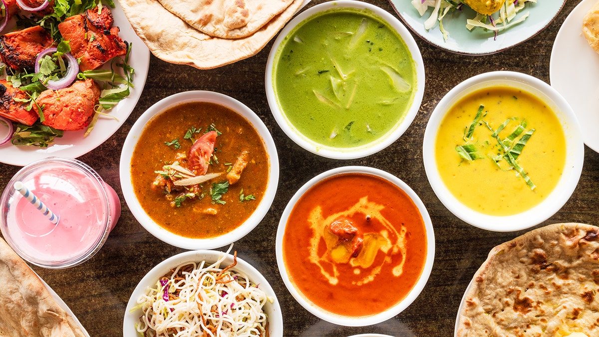 A variety of colorful Indian dishes including curries, naan, rice, and salads on a table.