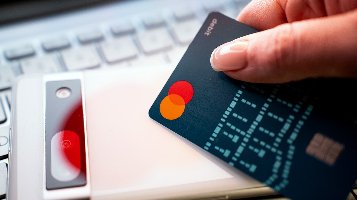 A person holds a debit card next to a mobile phone.