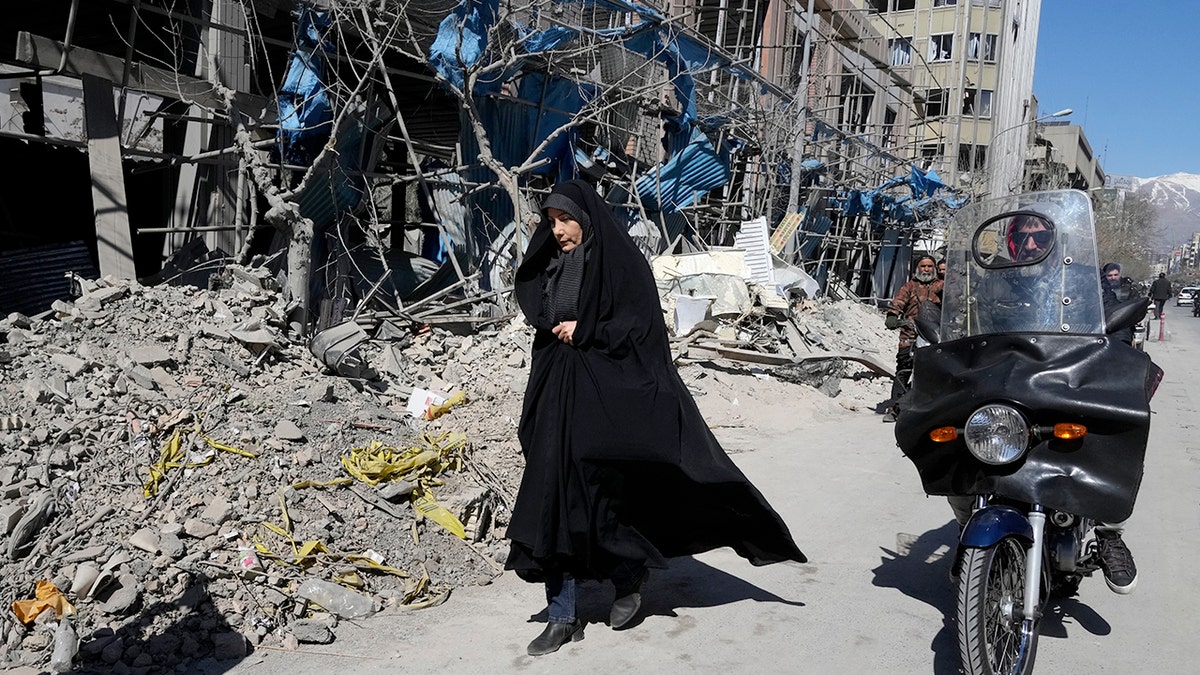 A woman walks by rubble in Iran