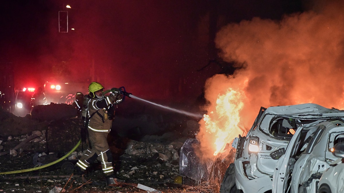 A firefighter spraying water on a burning car in a debris-filled street in Tel Aviv.