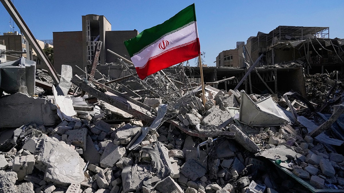An Iranian flag standing upright in the rubble of a demolished building.