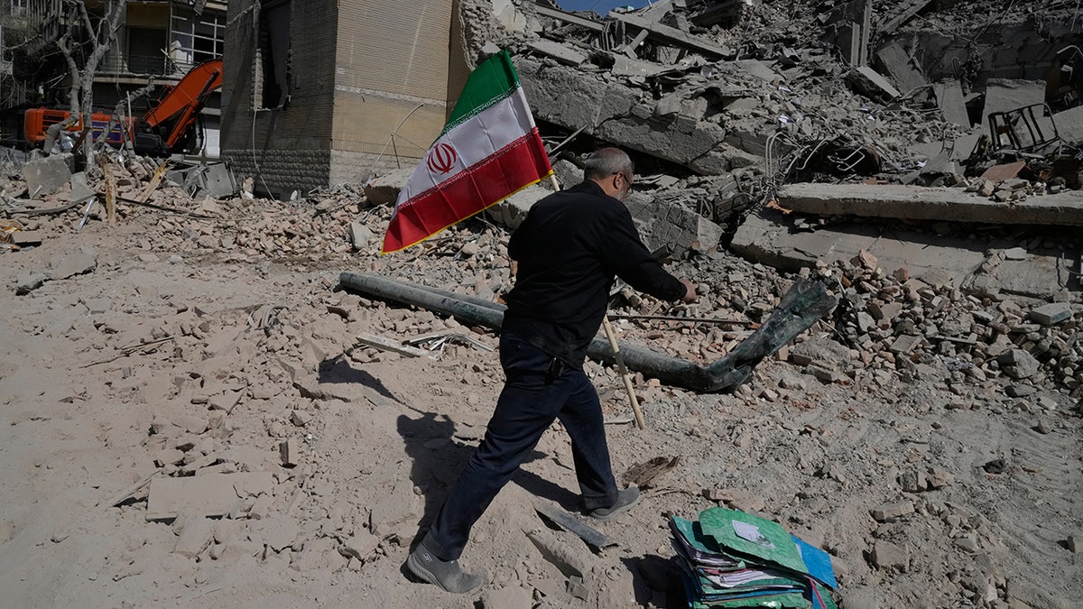 A man carrying an Iranian flag toward the rubble of a police facility in Tehran, Iran.