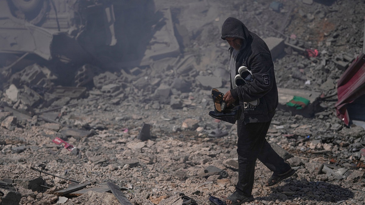 A man carrying shoes while standing in the ruins of a destroyed house.