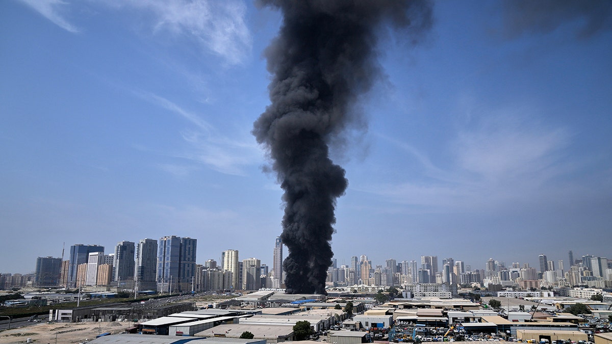 A thick black plume of smoke billowing from an industrial warehouse in Sharjah.