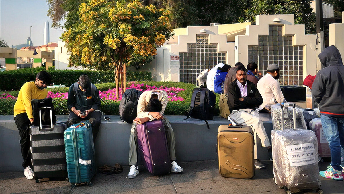 Passengers waiting with their luggage in an outdoor airport parking lot in Dubai.