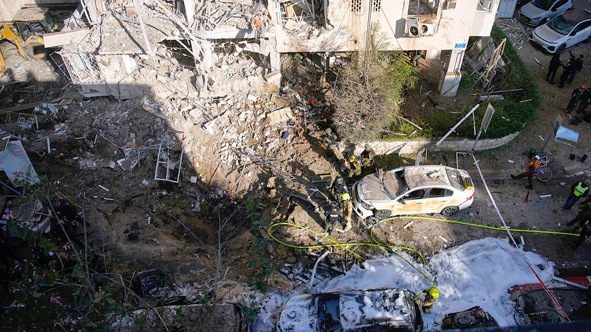 Israeli security forces and rescue teams inspecting a large crater and damaged buildings on a city street.