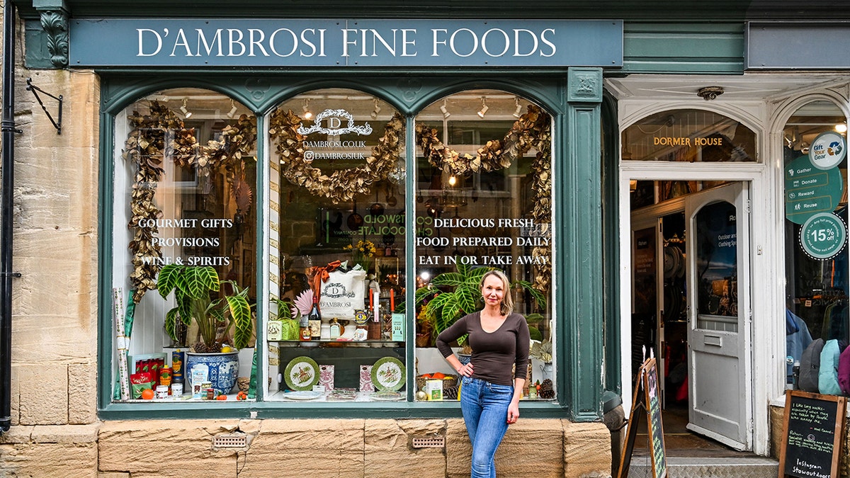Jesse D'Ambrosi standing outside D’Ambrosi Fine Foods shop with gourmet food display in a Cotswold village storefront.